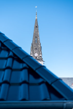 Behind a roof with dark blue shimmering tiles a church tower appearsの写真素材