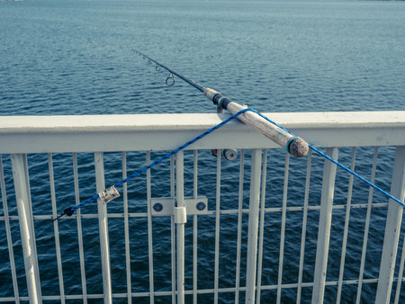 A fishing rod is attached to a bridge handrail over a lake.の写真素材