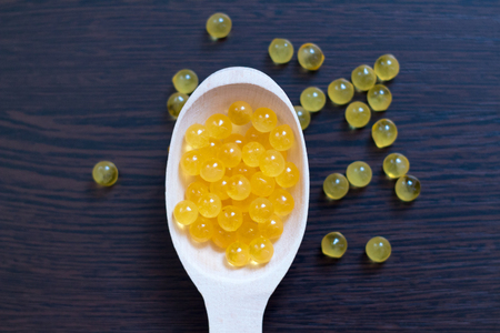 Fish oil. Cod liver oil omega 3 gel capsules. Granules in a wooden spoon on a dark backgroundの写真素材