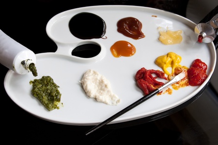 A palette-shaped plate with pastes & sauces and paintbrush depicting a creative approach to foodの写真素材