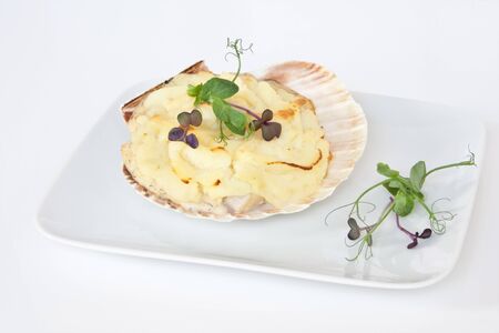 Coquilles Saint Jacques, a typical French dish consiting of scallops, prawns & fish in a creamy sauce topped with mashed potato ans garnished with pea shoots & radish cressの写真素材