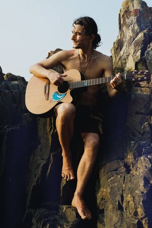 guitarman sitting with guitar in front of the sky with rockの写真素材