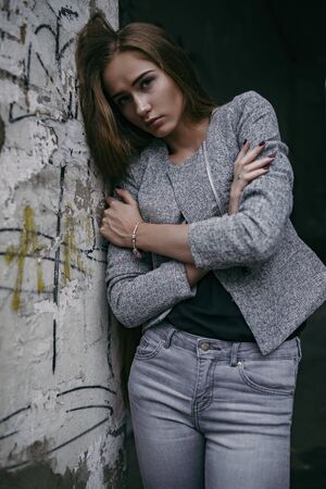 Girl in grey suit posing beside grey wallの写真素材