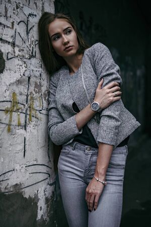 Girl in grey suit posing beside grey wallの写真素材