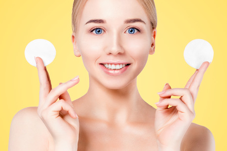 Beautiful spa model looking at camera while standing against yellow background. Beautiful face with fresh sweets. Facial treatment.の写真素材