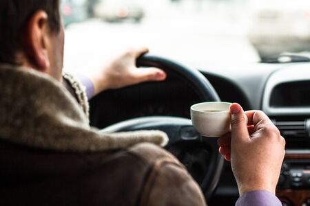 A man sitting in a car and holding a cup of coffeeの写真素材