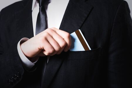 businessman put or take out credit card in pocket, close up on a gray backgroundの写真素材