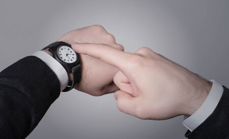 Man's hand in the suit pointing on his watch on a gray backgroundの写真素材