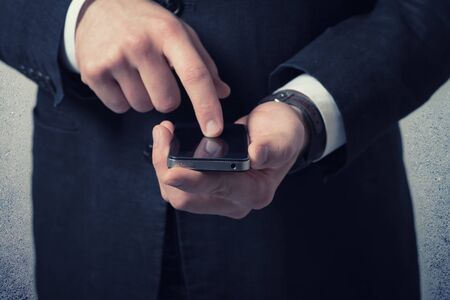Close up of young businessman using smart phone on gray backgroundの写真素材