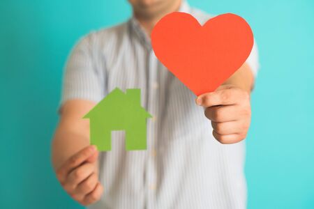 man with glasses holding a heart and a small house in the hands ofの写真素材