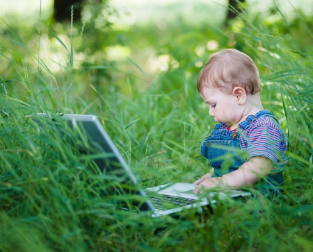 little boy playing outdoors with a laptopの写真素材