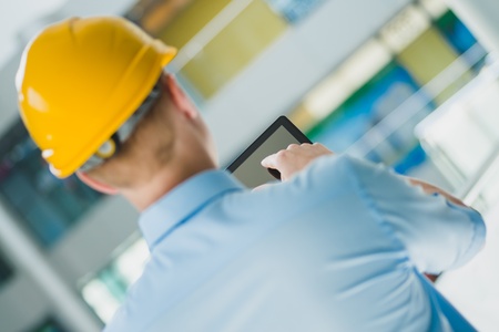 Young successful engineer in a helmet with a digital tablet