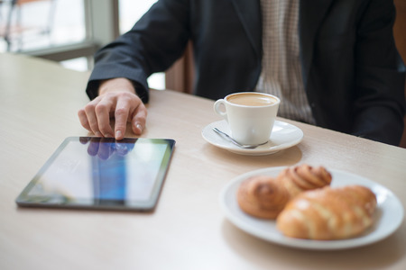 Man with tablet computer reading news at motning in cafeの写真素材