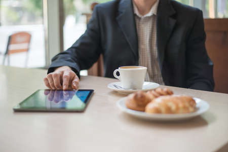 Man with tablet computer reading news at motning in cafeの写真素材