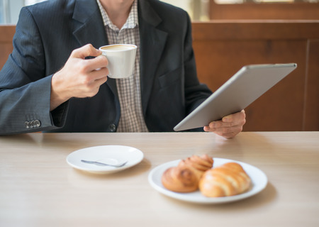 Man with tablet computer reading news at motning in cafeの写真素材