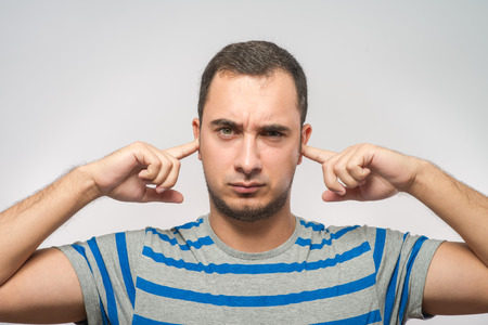 Closeup portrait young, angry, unhappy, stressed man covering his earsの写真素材
