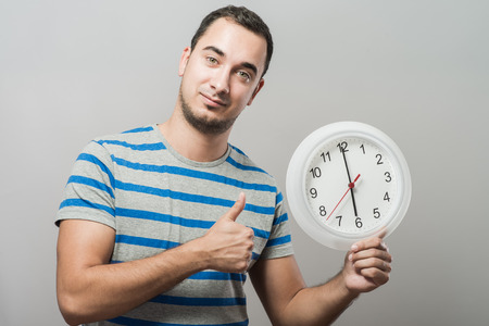 Time is money! Serious young man holding a clock in his handの写真素材