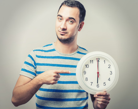 Time is money! Serious young man holding a clock in his handの写真素材