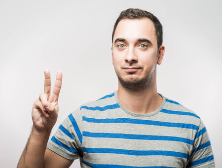 young casual man showing the victory gesture while smilingの写真素材