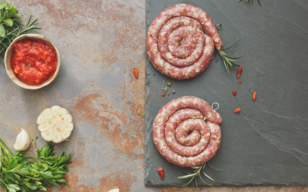 Raw sausages. Raw uncooked gourmet sausages with rosemary with rosemary and spices on a rustic background. Overhead view, vintage toned image, blank spaceの写真素材