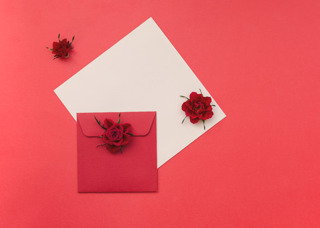 Natural  roses flowers and envelope on red paper background. Top view, blank space