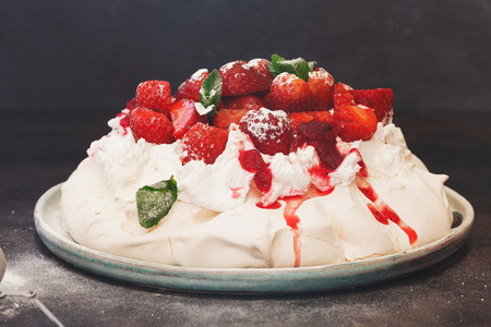 Delicious pavlova cake topped with sweetened whipped cream, balsamic strawberries and cranberry sauce, selective focusの写真素材