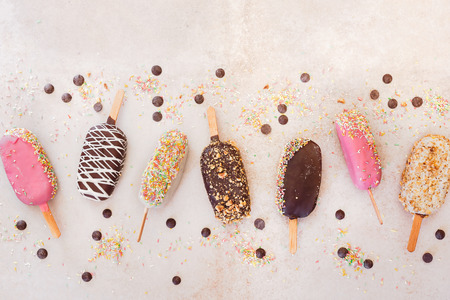 Ice cream sticks with chocolate, fruit, roasted almonds and colourful sugar sprinkles on rustic background. Top view, blank spaceの写真素材