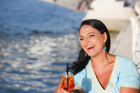 Happy beautiful tanning woman sitting  and drinking cocktail in seaside cafe, selective focusの写真素材