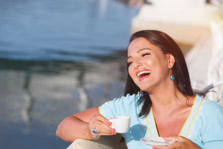 Beautiful happy woman drinking coffee on the pier at sunset. Vintage toned image, close upの写真素材
