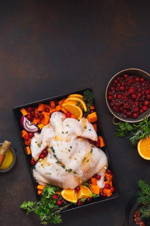 Preparing roast dinner with raw chicken and fresh herbs,  cranberries and orange slices. Top view, blank spaceの写真素材