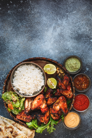 Smoky, roasted tandoori chicken wings served with pilau rice , soft garlic cheese naan with different chutney dipping sauces. Top view, blank space, rustic backgroundの写真素材
