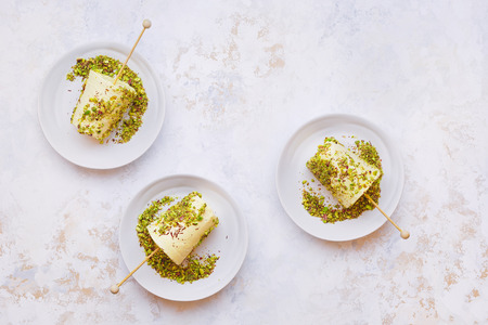 Cardamom and pistachio nut kulfi, Indian  ice cream served on white plates, textured surface. Top view, blank spaceの写真素材