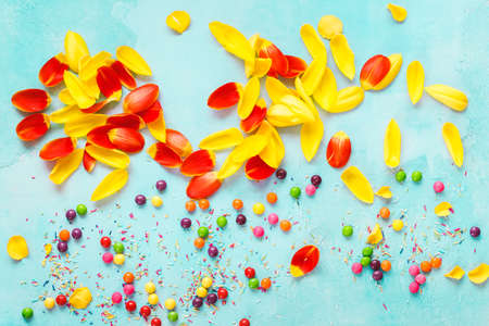 Easter composition on blue  background. Yellow and red tulips petal with multi colored candy background. Top view, blank spaceの写真素材