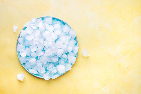 Heap Of Ice Cubes And Crushed Ice On Blue Plate From Above. Yellow  Background. Blank spaceの写真素材