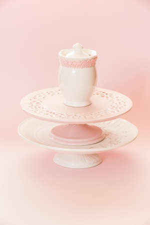 Empty white and pink cake stands and ceramic sugar pot, sugar serving bowl on top. Pink background with copy space, selective focusの写真素材