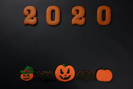 The hand-made eatable gingerbread 2020 inscription, Halloween pumpkins and bats on black backgroundの写真素材