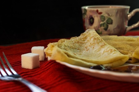 Pancakes with cherry jam, cutlery, sugar on a red background
