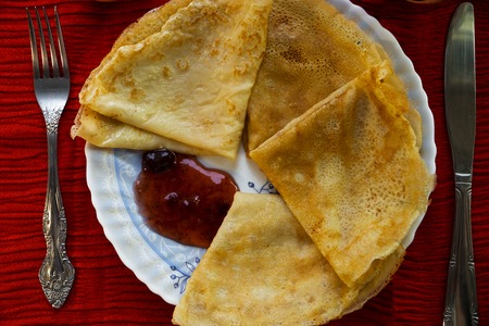 Pancakes with cherry jam and cutlery on a red background