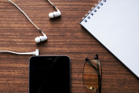 View of business have a phone, notebook, Goggles, headphones, pen and mobile phone with on wooden...