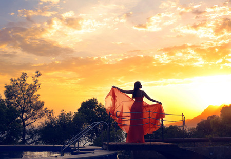 fabulous photo of beautiful sunset sky with woman in luxurious red dressの写真素材