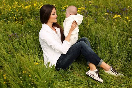 outdoor photo of beautiful mother with long dark hair having fun with her little cute baby in summer gardenの写真素材