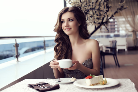 fashion outdoor photo of beautiful sensual woman with long dark hair in luxurious sequin dress posing in summer outdoor cafedrinking a coffeeの写真素材