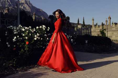 fashion outdoor photo of beautiful woman with dark hair wears luxurious red dress,posing in summer parkの写真素材