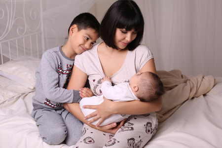 tender family photo of beautiful mother with short dark hair and her 2 children, having fun at cozy homeの写真素材