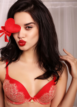 fashion interior photo of beautiful sexy girl with dark hair wears elegant lace lingerie, holding red heart, symbol of Valentine's dayの写真素材