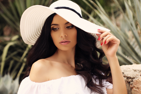fashion outdoor photo of gorgeous woman with dark hair in elegant white dress and hatの写真素材