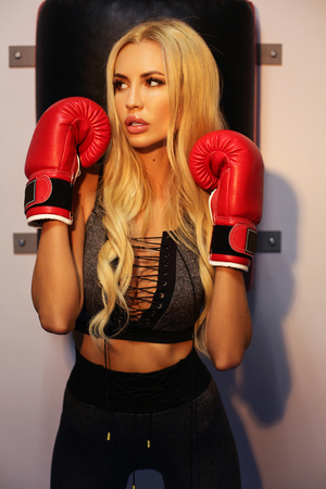 fashion photo of sexy woman with blond hair in sports clothes and boxer gloves, training in gymの写真素材