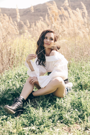 fashion outdoor photo of beautiful woman with dark hair in elegant clothes posing in spring field with reedsの写真素材