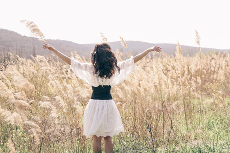 fashion outdoor photo of beautiful woman with dark hair in elegant clothes posing in spring field with reedsの写真素材