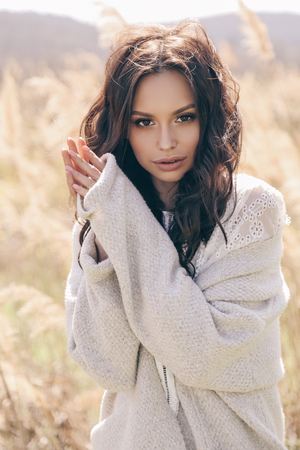 fashion outdoor photo of beautiful woman with dark hair in elegant clothes posing in spring field with reedsの写真素材
